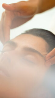 A person with closed eyes receives a relaxing facial massage from a pair of skilled hands. At Soneva Fushi, the environment is soft and tranquil, with a gentle light creating a calming atmosphere.
