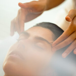 A person with closed eyes receives a relaxing facial massage from a pair of skilled hands. At Soneva Fushi, the environment is soft and tranquil, with a gentle light creating a calming atmosphere.