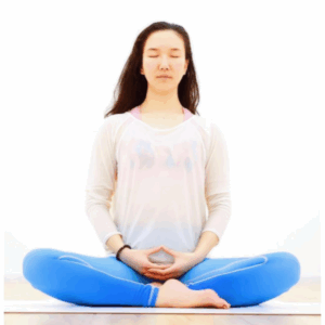 A woman in blue leggings and a white top sits cross-legged on a mat, eyes closed, with hands resting in her lap in a meditative pose—capturing the peaceful spirit of Soul at Soneva against a plain white background.