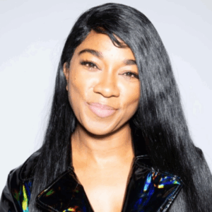 A woman with long, straight black hair smiles gently. She wears a shiny, black jacket and has a light, natural makeup look. The plain, light-colored background evokes the calming ambiance of Soul at Soneva.